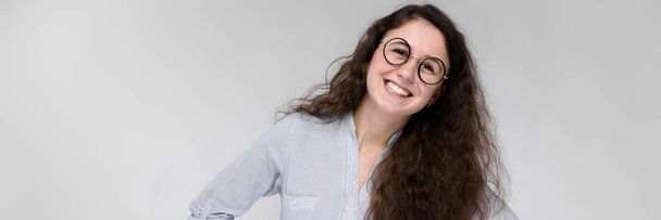 Portrait of a happy young girl in glasses. Beautiful young girl on a gray background. A young girl in a light blouse and dark trousers. - Fotografie, Obrázek