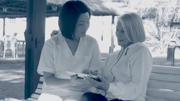 Nurse helping elderly woman using tablet on the bench. Sepia toned - Footage, Video