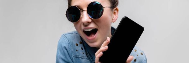 Young brunette girl in round glasses. Hairs are gathered in a bun. Girl with a black phone. - Photo, Image