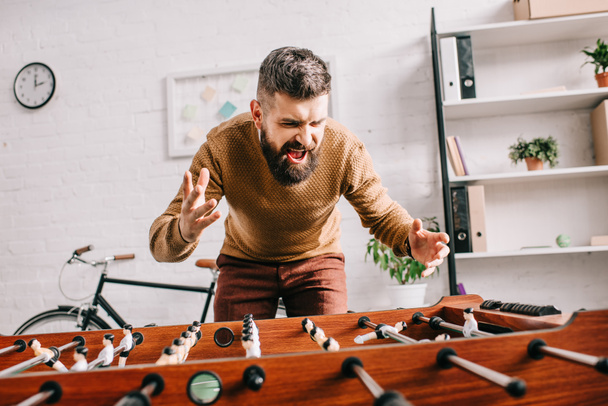 angry adult man yelling and playing table football game at home - Photo, Image