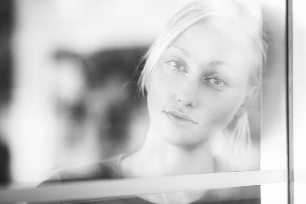 Černobílý záběr krásná blondýnka při pohledu na fotoaparát přes sklo - Fotografie, Obrázek