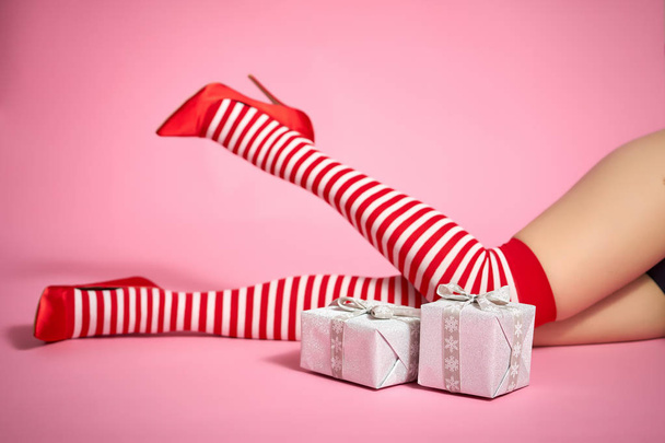sexy santa woman's legs on a bright pink background and Christmas gifts - Photo, image