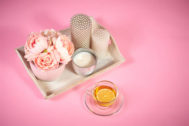 peonies λουλούδια, κεριά σε ένα ξύλινο δίσκο και το τσάι σε ένα ελαφρύ ροζ φόντο - Φωτογραφία, εικόνα