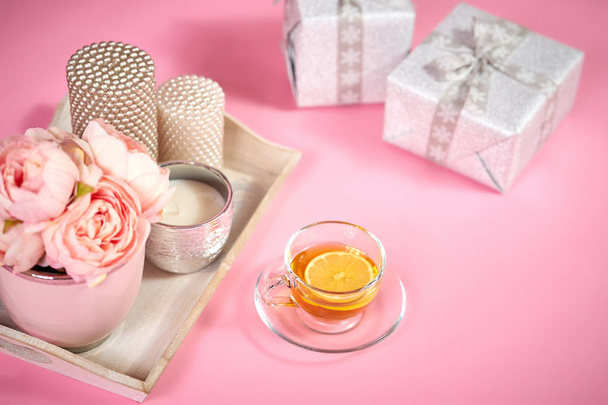 peonies, κεριά σε ένα ξύλινο δίσκο, τσάι και δώρα σε ένα ελαφρύ ροζ φόντο - Φωτογραφία, εικόνα