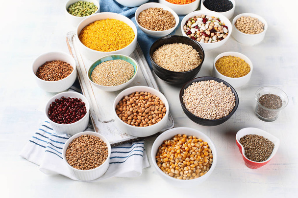 Various grains, cereals, seeds and beans in bowls on table. - Фото, изображение