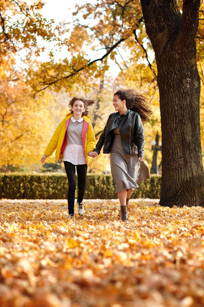 Two happy girls running in autumn city park. - Photo, Image