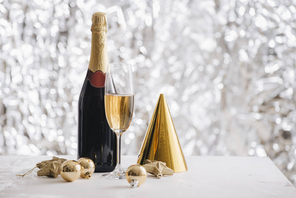 シャンパン グラスとシルバーのキラキラ背景に紙の帽子とクリスマス飾り瓶 - 写真・画像