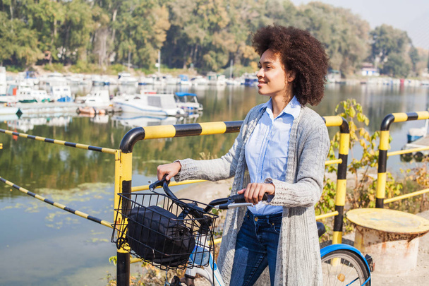 Femme afro détendue avec vélo profitant de temps libre près de la rivière
. - Photo, image