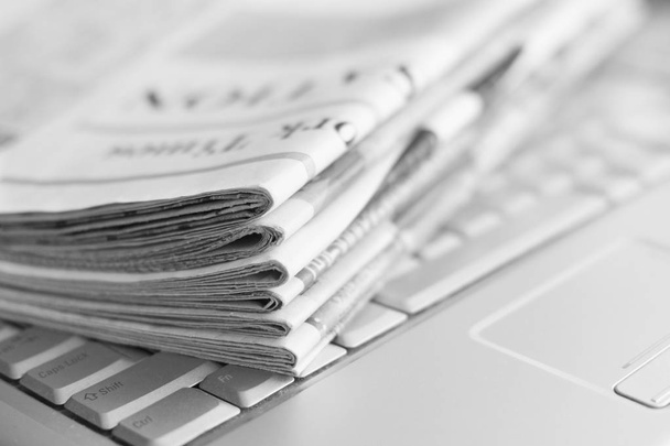 Newspapers and laptop. Pile of daily papers with news on the computer. Pages with headlines, articles folded and stacked on keypad of electronic device. Modern gadget and old journals, focus on paper  - Фото, зображення