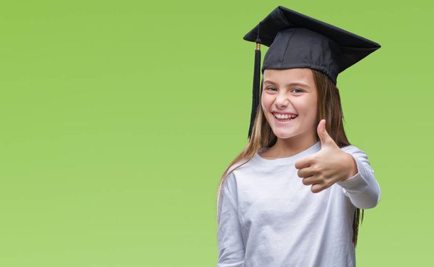 Young beautiful girl wearing graduate cap over isolated background doing happy thumbs up gesture with hand. Approving expression looking at the camera with showing success. - Fotoğraf, Görsel