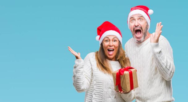 Hispánský pár středního věku nosí vánoční čepice a hospodářství dar nad, samostatný pozadí velmi šťastný a nadšený, vítěz výraz slaví vítězství křičet s velkým úsměvem a pozvedl ruce - Fotografie, Obrázek
