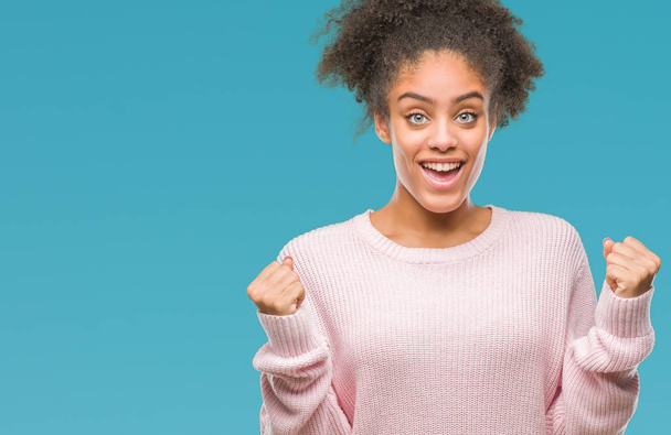 Mujer afroamericana joven con suéter de invierno sobre fondo aislado celebrando sorprendida y sorprendida por el éxito con los brazos levantados y los ojos abiertos. Concepto ganador
. - Foto, imagen