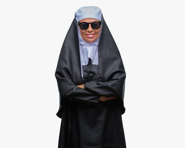 Middle age senior catholic nun woman wearing sunglasses over isolated background happy face smiling with crossed arms looking at the camera. Positive person. - Photo, Image