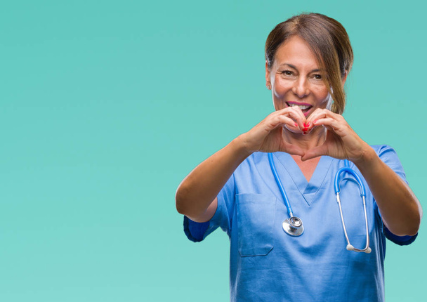Keski-ikäinen vanhempi sairaanhoitaja lääkäri nainen yli eristetty tausta hymyilee rakkaudessa osoittaa sydämen symboli ja muoto käsin. Romanttinen käsite
. - Valokuva, kuva
