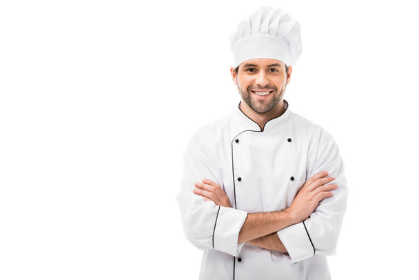 Lächelnder junger Koch mit verschränkten Armen, der isoliert auf weiß in die Kamera blickt - Foto, Bild