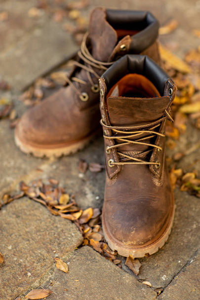 Brown leather boots stand on the floor with autumn dry leaves. Hipster shoes. Autumn Mood - Zdjęcie, obraz