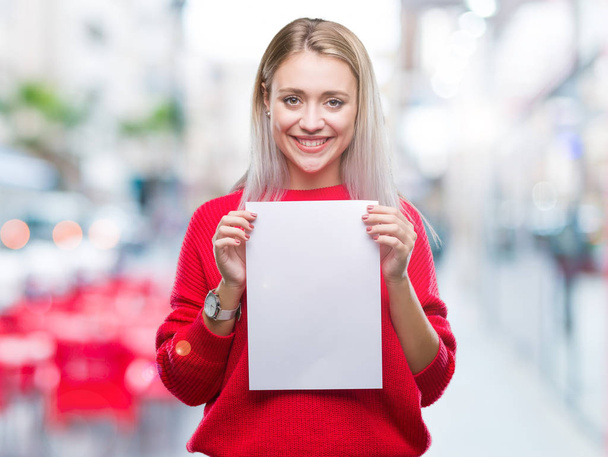 Mulher loira jovem segurando folha de papel em branco sobre fundo isolado com um rosto feliz de pé e sorrindo com um sorriso confiante mostrando dentes
 - Foto, Imagem