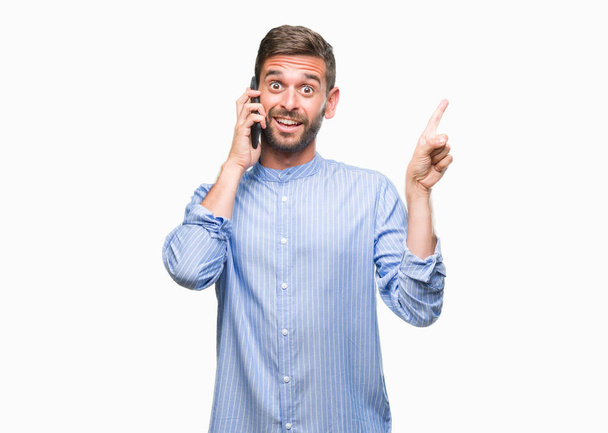 Όμορφος νεαρός μιλώντας στο τηλέφωνο πάνω από απομονωμένες φόντο πολύ χαρούμενος, δείχνοντας με το χέρι και δάχτυλο προς την πλευρά - Φωτογραφία, εικόνα