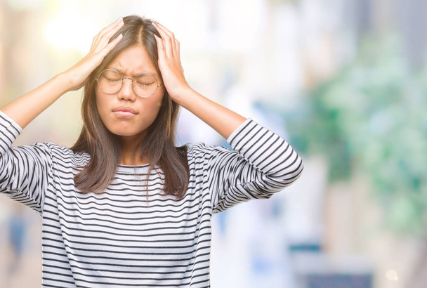 Mujer asiática joven con gafas sobre un fondo aislado que sufre de dolor de cabeza desesperado y estresado porque el dolor y la migraña. Manos en la cabeza
. - Foto, Imagen