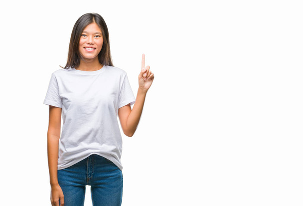 Joven asiática mujer sobre aislado fondo mostrando y apuntando hacia arriba con dedo número uno mientras sonríe confiado y feliz
. - Foto, imagen