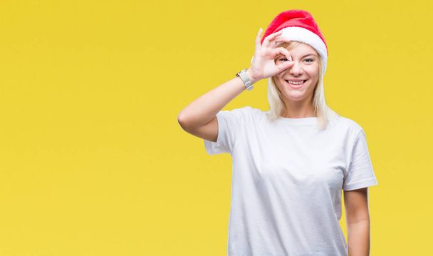 手の笑顔、幸せそうな顔で指を通して見る目で ok のジェスチャーを行う分離の背景にクリスマスの帽子をかぶって若い美しいブロンドの女性. - 写真・画像