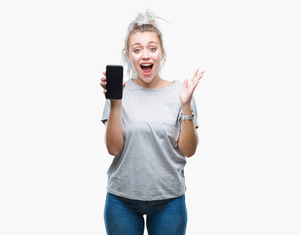 Молодая блондинка показывает экран смартфона на изолированном фоне очень счастливый и взволнованный, победитель выражение празднования победы кричит с большой улыбкой и поднятыми руками
 - Фото, изображение