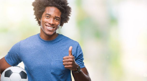 Afro american man holding football ball over isolated background happy with big smile doing ok sign, thumb up with fingers, excellent sign - Φωτογραφία, εικόνα