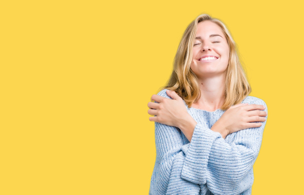 Hermosa mujer joven con suéter azul sobre un fondo aislado abrazándose feliz y positivo, sonriendo confiado. Amor propio y cuidado personal
 - Foto, Imagen