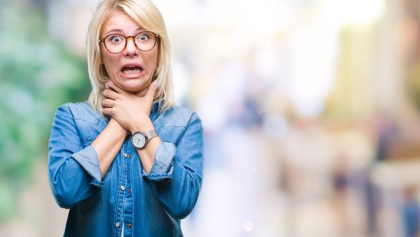 Young beautiful blonde woman wearing glasses over isolated background shouting and suffocate because painful strangle. Health problem. Asphyxiate and suicide concept. - Photo, Image