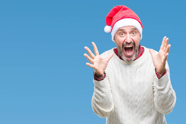 中年白髪年配の男性にクリスマスの帽子をかぶって狂気を祝う背景を分離した腕を上げると成功のためびっくりし、叫んで興奮して目を開きます。勝者の概念 - 写真・画像