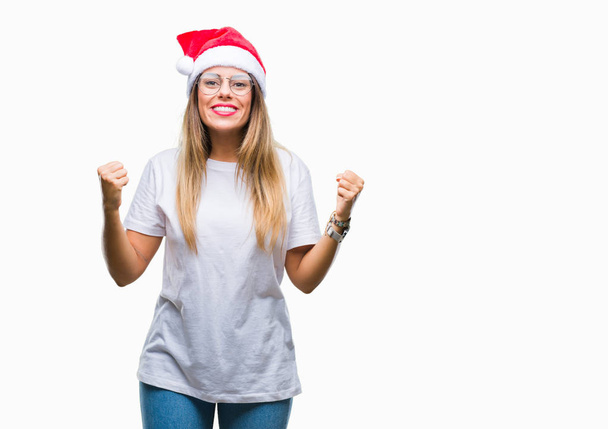 Young beautiful woman wearing christmas hat over isolated background celebrating surprised and amazed for success with arms raised and open eyes. Winner concept. - 写真・画像