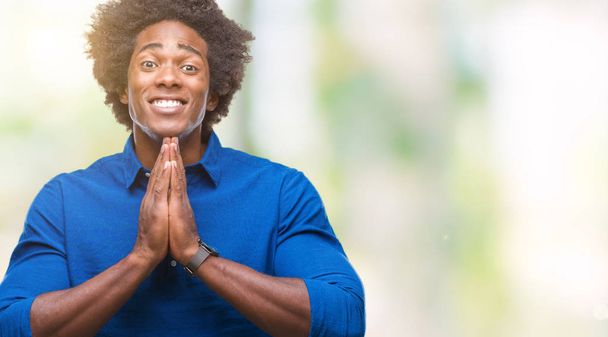 Hombre afroamericano sobre fondo aislado rezando con las manos juntas pidiendo perdón sonriendo confiado
. - Foto, Imagen
