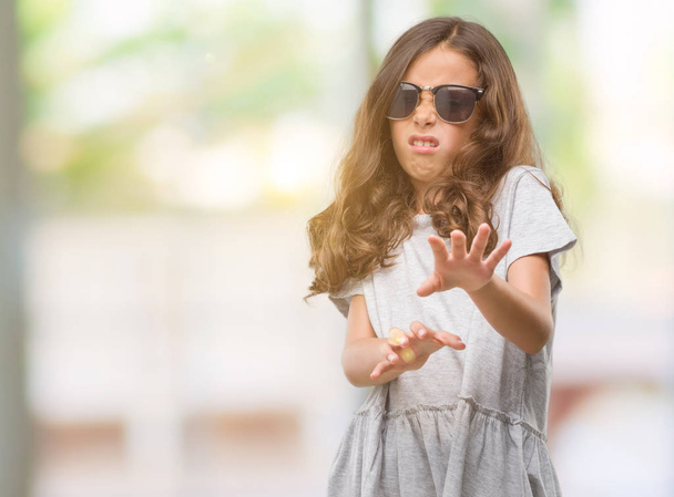brünettes hispanisches Mädchen mit Sonnenbrille angeekelten Ausdruck, ungehalten und ängstlich dabei Ekel Gesicht, weil Abneigung Reaktion. mit erhobenen Händen. Ärgerliches Konzept. - Foto, Bild