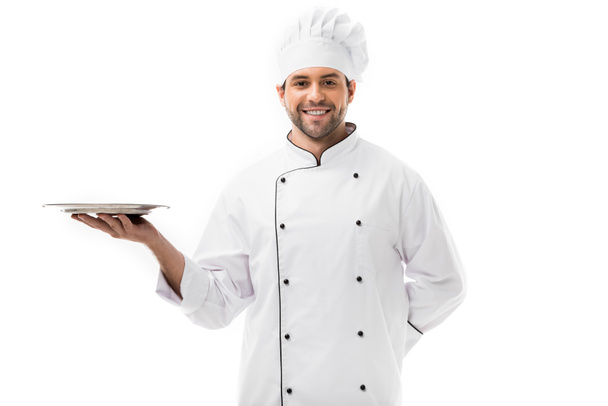 Lächelnder junger Koch mit leerem Teller und Blick in die Kamera isoliert auf Weiß - Foto, Bild