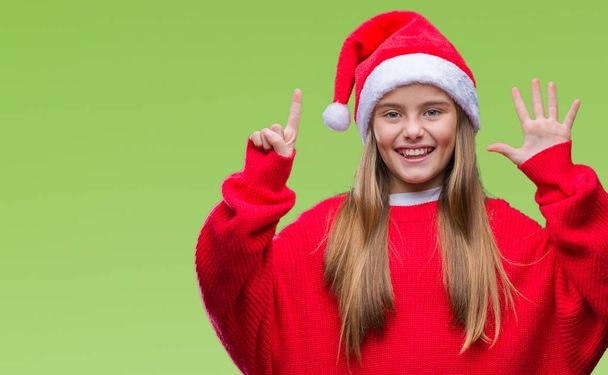 junges schönes Mädchen mit Weihnachtsmütze über isoliertem Hintergrund zeigt und zeigt mit Fingern Nummer sechs, während sie selbstbewusst und glücklich lächelt. - Foto, Bild