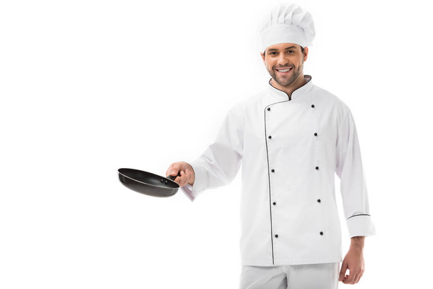sonriente joven chef sosteniendo sartén y mirando a la cámara aislada en blanco
 - Foto, Imagen