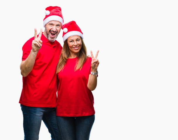 Středním věku hispánský pár klobouk vánoční izolované pozadí usmívající se smajlík, mrkl na fotoaparát dělá znamení vítězství. Číslo dvě. - Fotografie, Obrázek