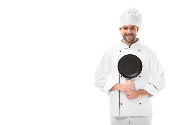 happy young chef holding frying pan and looking at camera isolated on white - Foto, afbeelding