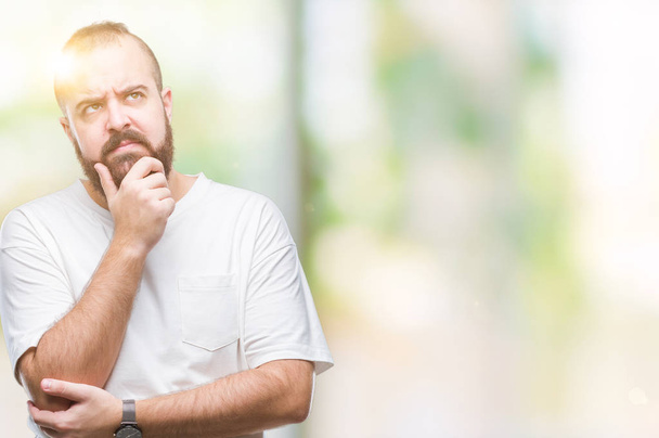 Young caucasian hipster man wearing casual t-shirt over isolated background with hand on chin thinking about question, pensive expression. Smiling with thoughtful face. Doubt concept. - Foto, immagini