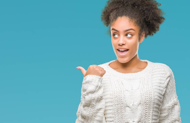 Młody afro american kobieta swetrze zima na białym tle uśmiechnięty z szczęśliwy twarz patrząc i skierowaną do boku z kciukiem w górę. - Zdjęcie, obraz