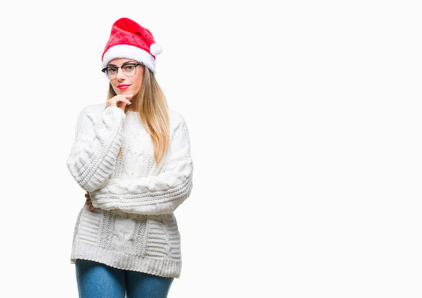 Молода красива жінка в різдвяному капелюсі над ізольованим тлом з рукою на підборідді думає про питання, стомлююче вираження. Посміхаючись з розсудливим обличчям. Концепція сумніву
. - Фото, зображення
