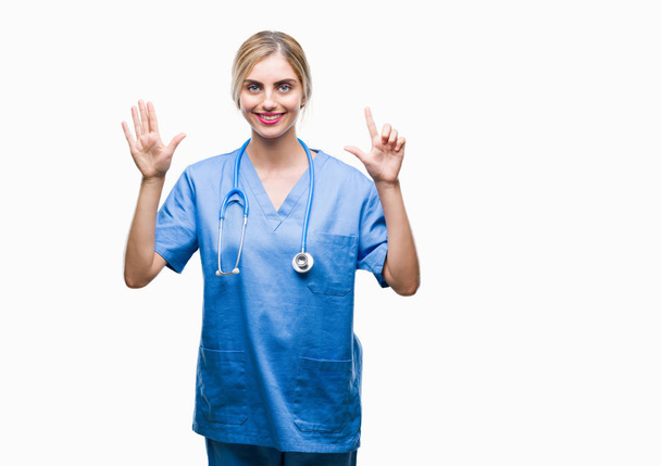 Giovane bella bionda medico chirurgo infermiera donna su sfondo isolato mostrando e indicando con le dita numero sette sorridendo fiducioso e felice
. - Foto, immagini