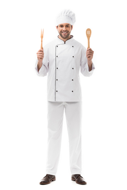 sonriente joven chef sosteniendo utensilios de cocina y mirando a la cámara aislada en blanco
 - Foto, Imagen