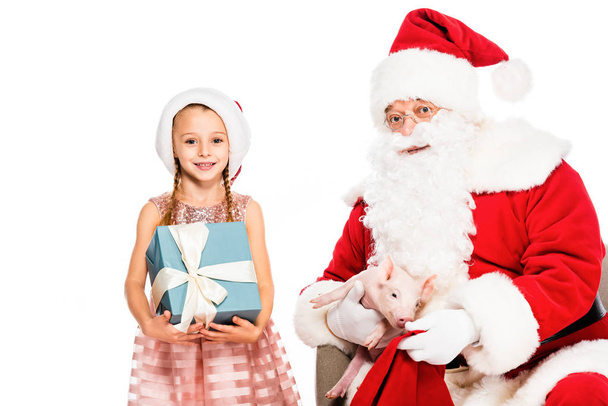 Père Noël Claude et petit enfant regardant la caméra tout en tenant le cochon et boîte cadeau isolé sur blanc
 - Photo, image