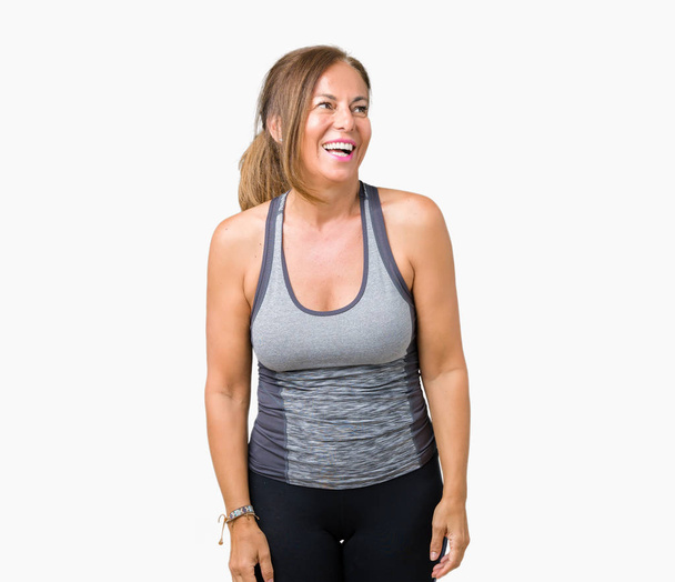 Beautiful middle age woman wearing sport clothes over isolated background looking away to side with smile on face, natural expression. Laughing confident. - Photo, Image