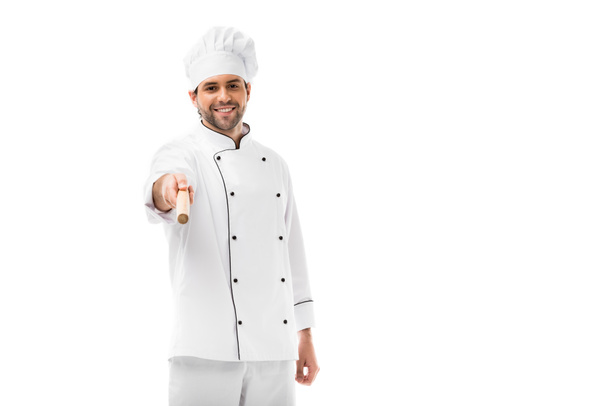 handsome young chef holding rolling pin and pointing at camera isolated on white - Photo, Image