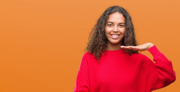 Young hispanic woman wearing red sweater gesturing with hands showing big and large size sign, measure symbol. Smiling looking at the camera. Measuring concept. - Foto, afbeelding