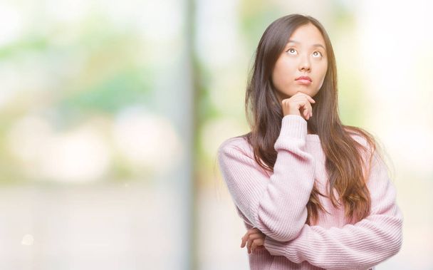 Young asian woman over isolated background with hand on chin thinking about question, pensive expression. Smiling with thoughtful face. Doubt concept. - Фото, зображення