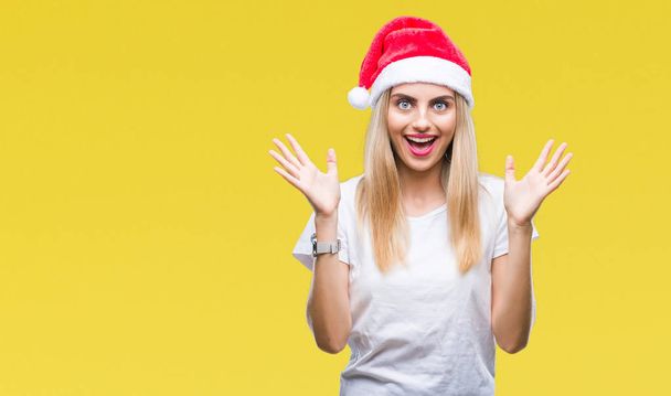 以上若い金髪美人クリスマス帽子クレイジーを祝う背景を分離した腕を上げると成功のためびっくりし、叫んで興奮して目を開きます。勝者の概念 - 写真・画像