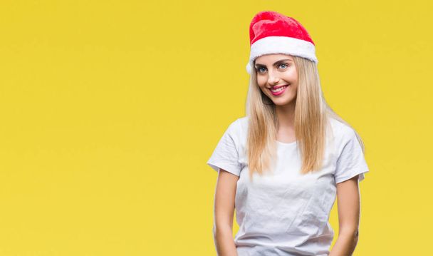 junge schöne blonde Frau Weihnachtsmütze über isoliertem Hintergrund, die mit einem Lächeln im Gesicht, natürlichem Ausdruck zur Seite schaut. Lachen selbstbewusst. - Foto, Bild